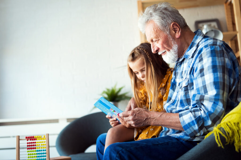 Grandfather and granddaughter sitting on couch, reading a book together
