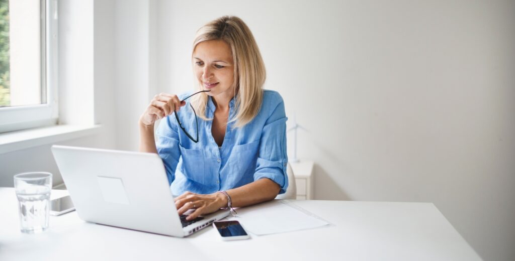Woman sitting at desk, looking at computer, and reviewing insights about stock market volatility. 
