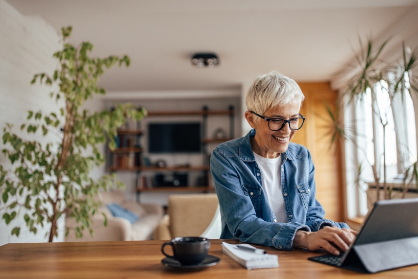Smiling older woman sitting at desk typing on iPad, finding ways to minimize her tax burden