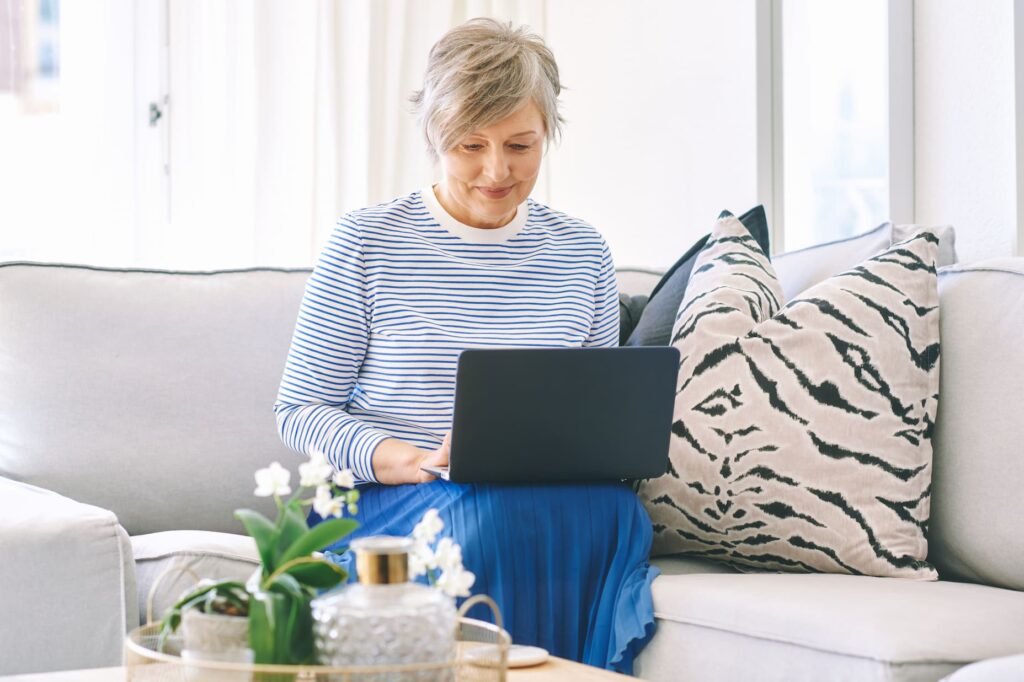 Older woman sitting on a couch, looking at her laptop, reviewing the Fed rate cut announcement.